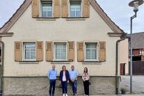 Vier Vertreterinnen und Vertreter von Gemeinde und interkommunaler Allianz sowie von Denkmalpflege und ländlicher Entwicklung vor einem im traditionellen fränkischen Baustil errichteten, sanierungsbedürftigen Haus.
