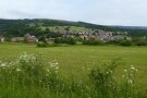 Ein Dorf liegt inmitten von viel Grün. Im Hintergrund flache Begkuppen.