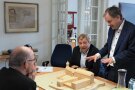 Bischof und Amtsleiter schauen auf ein Gebäudemodell, während eine dritte Person gewissermaßen mit seinen Händen spricht.