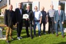Auf der Rasenfläche vor dem Dorfgemeinschaftshaus stehen sieben Männer. Der zweite von links bekommt einen Teller mit bayerischem Staatswappen überreicht.