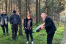 Anschaulich erläutert Diplomforstwirt Bernd Günzelmann der Staatssekretärin Dr. Manuela Rottmann aus dem Bundeslandwirtschaftsministerium, warum und wo Handlungsbedarf beim Wald in Unterfranken besteht. Weitere Personen verfolgen den Vortrag im lichten Wald.