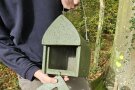 Jemand hält einen Vogelnistkasten, dessen Vorderwand er herausgenommen hat.
