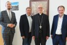 Vier Herren lächeln in die Kamera. Einer von ihnen trägt ein etwa zehn Zentimeter großes Brustkreuz.