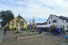 Am Rand eines mit Bäumen und Sträuchern sowie Sitzgelegenheiten gegliederten Platzes ist ein Festzelt aufgebaut. Darin und davor herrscht reger Betrieb.