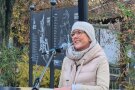 Eine lächelnde Frau spricht in ein Mikrofon. Sie steht an einem großen Schild, das eine Übersicht zeigt, welche Stationen auf dem neuen Bücholder Rundweg angesteuert werden