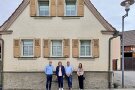 Vier Vertreterinnen und Vertreter von Gemeinde und interkommunaler Allianz sowie von Denkmalpflege und ländlicher Entwicklung vor einem im traditionellen fränkischen Baustil errichteten, sanierungsbedürftigen Haus.