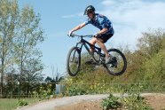 Ein Jugendlicher macht mit seinem Geländefahrrad einen mächtigen Sprung. Die Reifen befinden sich einen guten Meter über der planierten Piste.