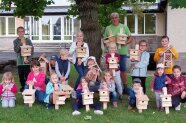 Mädchen und Jungen zeigen gemeinsam mit ihrem Anleiter die Nistkästen, die sie aus Lärchenholz zusammengebaut haben.