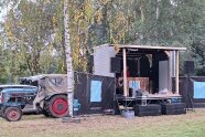 Ein Traktor hat einen Anhänger mit Spezialaufbau auf eine Wiese gezogen. Die einstige Ladefläche ist jetzt die Bühne einer Band.
