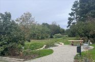 Der Bachlauf ist sauber mit Natursteinen eingefasst, sodass der Zugang zum Wasser immer frei ist. Nebenan stehen auf einem geschotterten Platz Bänke und ein Tisch zum Rasten.