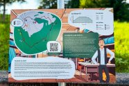 Eine Infotafel zeigt eine Wanderroute, das Höhenprofil und einen Schneider vor einem Regal mit Stoffballen. Ein QR-Code bietet die Möglichkeit, sich mittels Smartphone berichten zu lassen, welche Rolle das Schneiderhandwerk in der Gegend spielte und noch spielt.