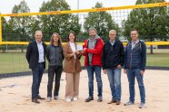 Eine Frau und fünf Männer mit strahlenden Gesichtern auf einem Beachvolleyballfeld. Bei der Inbetriebnahme desselben hielten sie einen Förderhinweis der ILE Mainschleife Plus in die Kamera.