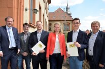 Sechs Personen stehen am Eingang zum Amtsgebäude. Zwei halten eine Urkunde in ihren Händen.