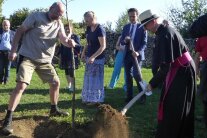 Bischof Dr. Franz Jung schaufelt Erde auf die Wurzeln eines Obstbaums.