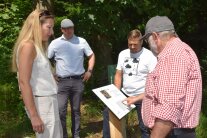 Vier Personen scharen sich um eine Infotafel über die Baumart Eibe.