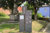 Ein idyllisches Plätzchen im Schatten hoher Bäume und eines Ehrenmals. Hier hat der Verein „Harter Kern 2.0“ drei Metallstelen aufgestellt, um über die Geschichte des Dorfes Brünnau zu informieren.