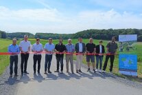 Eine Gruppe von Menschen ist entlang eines roten Stoffbandes aufgereiht, um dieses zu durchschneiden und damit zwei neu ausgebaute Wege freizugeben.
