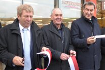 Bayerns Ministerpräsident Markus Söder (von rechts), Retzstadts Bürgermeister Karl Gerhard sowie Jürgen Eisentraut, der Leiter des Amtes für Ländliche Entwicklung Unterfranken, halten ihren jeweiligen Abschnitt eines weiß-roten Bandes in Händen, das sie durchschnitten, um so symbolisch das „Retschter Lädchen“ zu eröffnen.