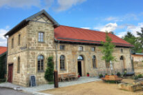 Saniertes Brauhaus in Köslau. Auf dem Vorplatz steht ein neu gepflanzter Baum mit Rundbank, daneben ein Steintrog