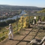 Blick vom Fränkischen Rotwein Wanderweg auf das Maintal bei Erlenbach mit den steilen Weinbergslagen. Eine Frau blickt ins Tal. Im Hintergrund sitzen zwei Personen unter einer Metallpergola an einer Tisch-Bank-Garnitur