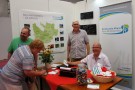 Achim Müller, Erster Bürgermeister der Gemeinde Birkenfeld und Günter Schmelz, Zweiter Bürgermeister des Marktes Karbach informieren am Messestand der Kommunalen Allianz Raum Marktheidenfeld zwei interessierte Besucherüber die Tätigkeit der Allianz. Im Hintergrund an der Wand Informationsplakate.