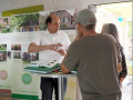 Ein Landschaftsarchitekt berät zwei Besucher zum Thema Grüngestaltung. Im Hintergrund Rollups der Ausstellung "DorfGrün gestalten"