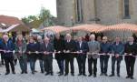 Die Ehrengäste, darunter Landrat Eberhard Nuß, Bürgermeister Burkard Losert, Domkapitular Dr. Helmut Gabel, Architekt Norbert Stieber und Robert Bromma vom Amt für Ländliche Entwicklung Unterfranken stehen auf dem Kirchplatz in einer Reihe und halten ein Band in Händen. Im Hintergrund die Kirche St. Afra