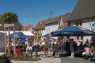 Der neue Dorfplatz von Holzkirchhausen. Es spielt eine Blaskapelle, rechts sitzen Gäste unter Sonnenschirmen und feiern die neue Ortsmitte