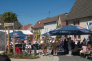 Der neue Dorfplatz von Holzkirchhausen. Es spielt eine Blaskapelle, rechts sitzen Gäste unter Sonnenschirmen und feiern die neue Ortsmitte