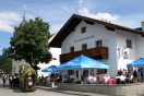 Altenauer Dorfwirtshaus mit Giebelfassade, vor der zahlreiche Gäste an Tischen sitzen. Auf der Straße Pferdegespann, das geschmückten Wagen mit Bierfässern zieht.